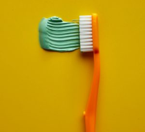 Orange toothbrush with green toothpaste on yellow background